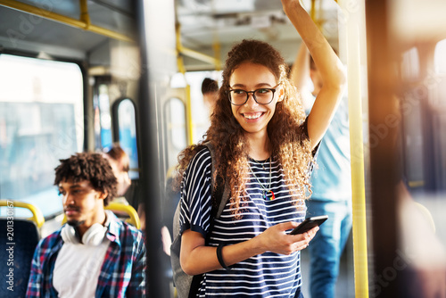 Young gorgeous cheerful woman is standing on the bus using the phone and smiling. photo