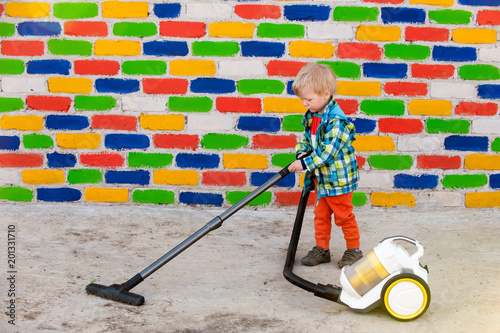 Happy child in bright suit with a vacuum cleaner against background of multi-colored brick wall. Romantic lighting with reflection of sunlight. Lens Flare effect without postproduction