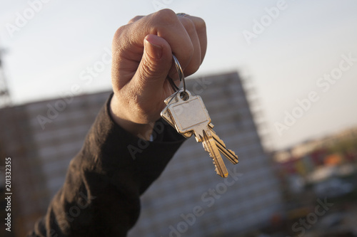 Mano de mujer sujetando unas llaves. Edificio en obras fuera de foco al fondo.