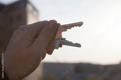 Mano de mujer sujetando dos llaves. Al fondo fuera de foco, un edificio. photo