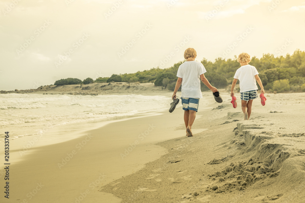 children walk barefoot on the shore at sunset in a swimsuit after a fun day of family games at the beach. Two happy boys playing on the beach on summer holidays enjoying nature with beautiful sea, snd children walk barefoot on the shore at sunset in a swimsuit after a fun day of family games at the beach. Two happy boys playing on the beach on summer holidays enjoying nature with beautiful sea, snd