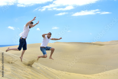 Happy friends jumping on the sand dunes.