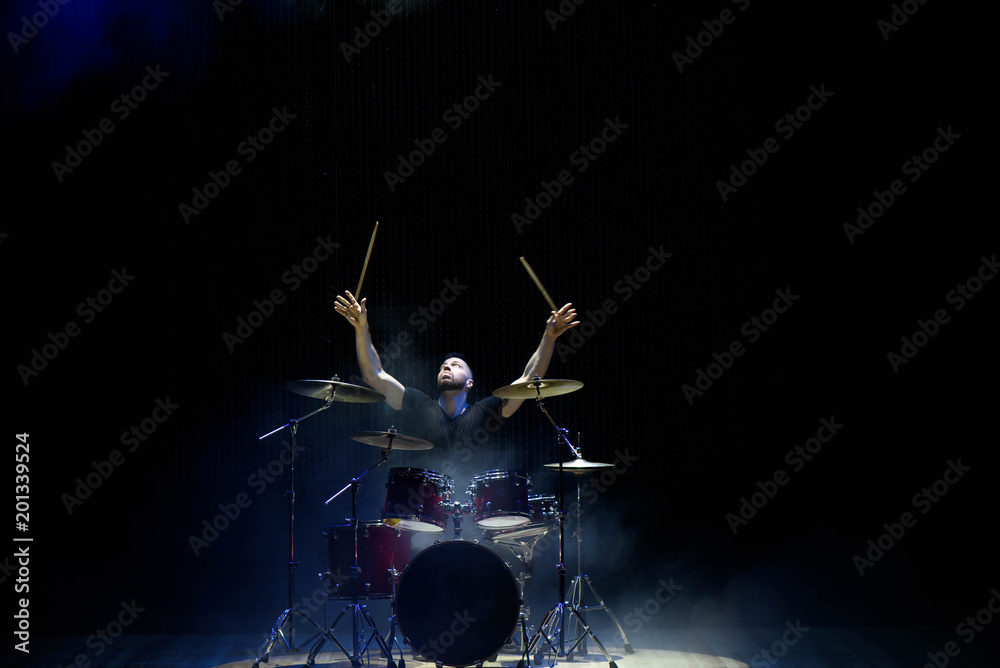 Obraz premium Drummer in a cap and headphones plays drums at a concert under white light in a smoke