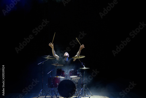 Photo Drummer in a cap and headphones plays drums at a concert under white light in a