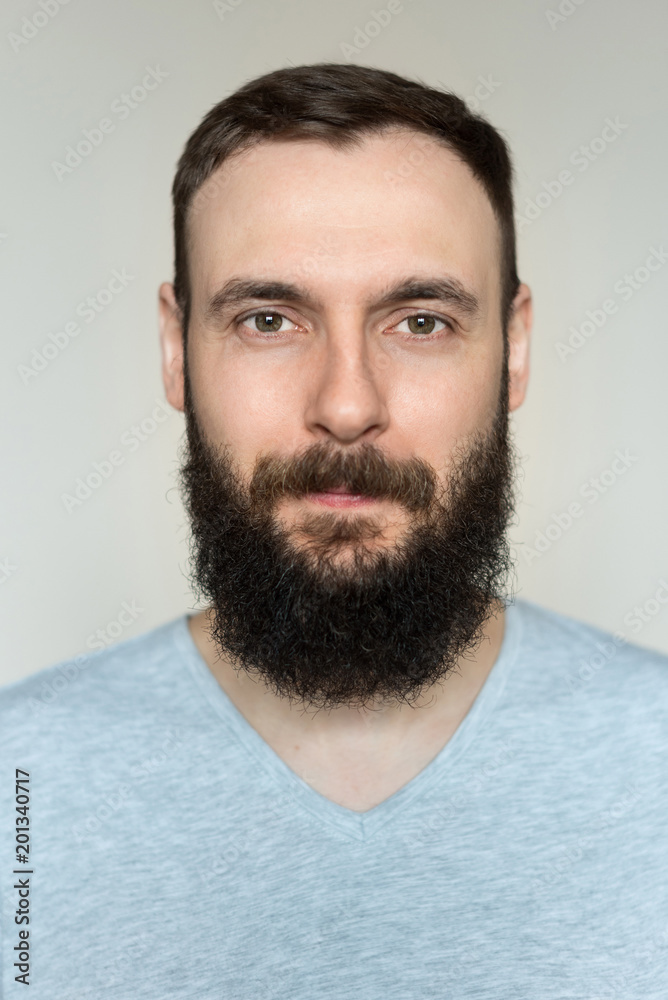 Portrait of a beautiful real hipster man with a full face of a beard and mustache on a light background in a barber shop in a gray shirt Portrait of a beautiful real hipster man with a full face of a beard and mustache on a light background in a barber shop in a gray shirt