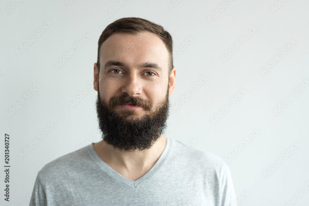 Portrait of a beautiful real hipster man with a full face of a beard and mustache on a light background in a barber shop in a gray shirt Portrait of a beautiful real hipster man with a full face of a beard and mustache on a light background in a barber shop in a gray shirt