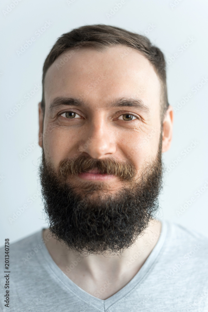 Portrait of a beautiful real hipster man with a full face of a beard and mustache on a light background in a barber shop in a gray shirt Portrait of a beautiful real hipster man with a full face of a beard and mustache on a light background in a barber shop in a gray shirt