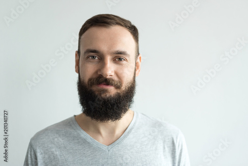 Portrait of a beautiful real hipster man with a full face of a beard and mustache on a light background in a barber shop in a gray shirt