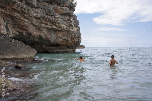 Boys swimming near some spurs of rocks at seashore