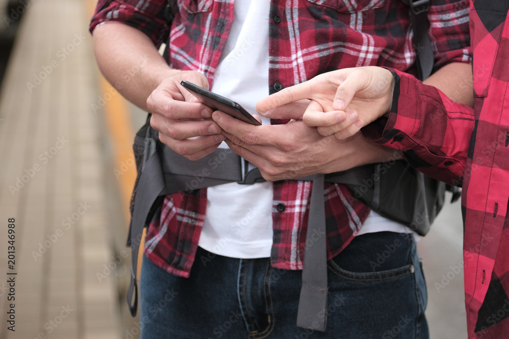 man & woman with backpack use app on smartphone at train station. traveler couple look at mobile phone. journey travel concept