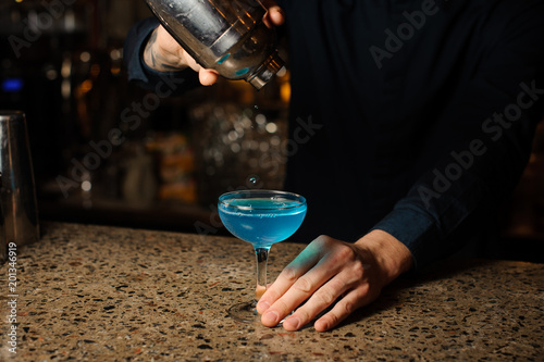 bartender pours the last drops of the alcoholic cocktail Blue Lagoon from the shaker