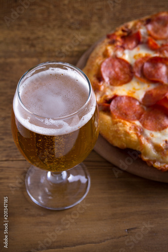 Beer and pepperoni pizza on wooden table. Glass of beer. Ale and food concept. vertical