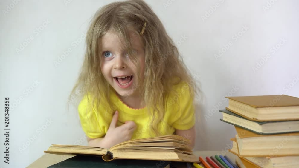 Small girl read books over table, then shows thumbs up. Cute beautiful children learning his lessons at home, back to school Small girl read books over table, then shows thumbs up. Cute beautiful children learning his lessons at home, back to school