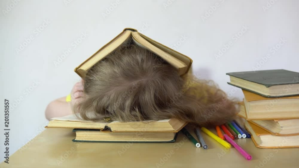 A small sweet blonde girl is sleeping on a book, she is tired when she did her homework. The child dreams of characters from the story.
