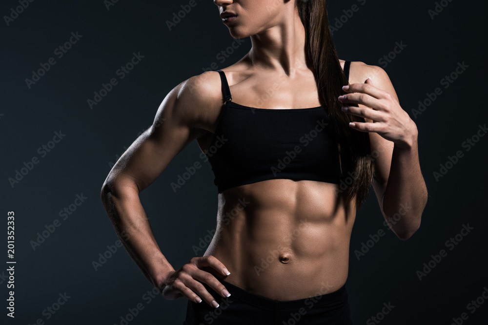 cropped view of sexy female bodybuilder posing in sportswear,  isolated on grey