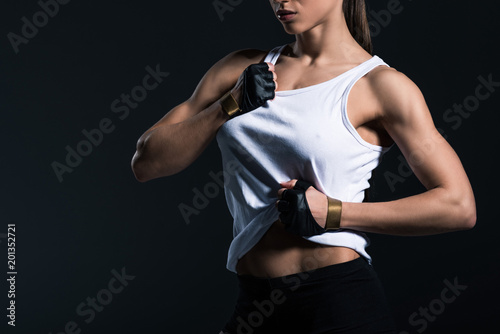 cropped view of muscular sportswoman showing abs, isolated on black © LIGHTFIELD STUDIOS
