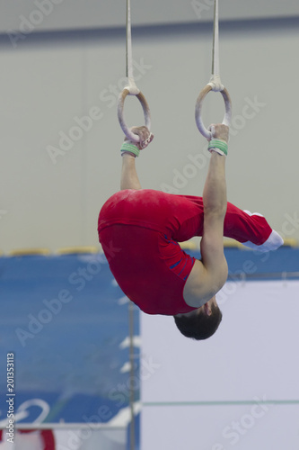 Athletic man performing with gymnastic rings at the competition