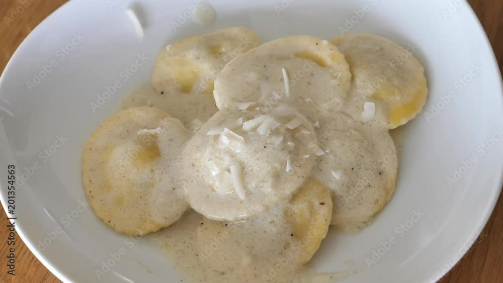 Slow motion - Shreds of Parmesan cheese fall on a plate of Ravioli Slow motion - Shreds of Parmesan cheese fall on a plate of Ravioli