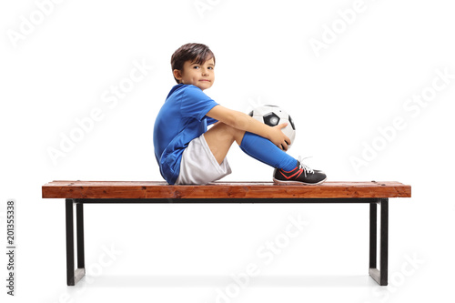 Little footballer sitting on a wooden bench and looking at the camera