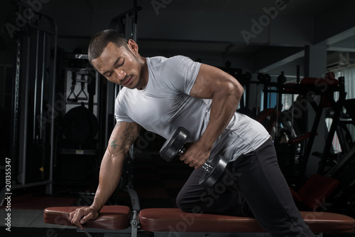 Muscular builder man training his body with dumbbell in Modern fitness center