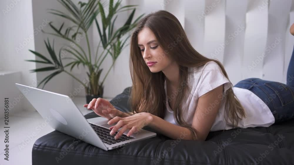 Attracitve young woman lying on her couch and typing on laptop, handheld Attracitve young woman lying on her couch and typing on laptop, handheld