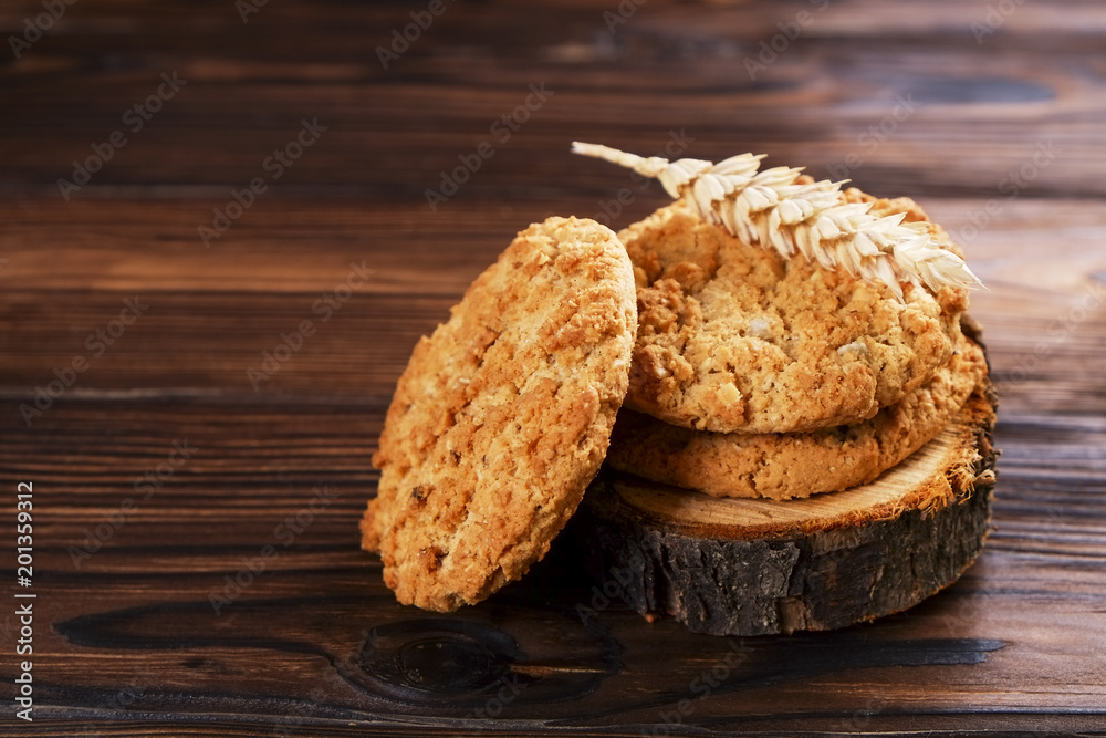 Healthy vegan integral cookies made of hazelnut powder on wooden slice coaster, wood table background. Home made vegetarian, gluten free snack with nuts. Decorative wheat spica. Close up, copy space. Healthy vegan integral cookies made of hazelnut powder on wooden slice coaster, wood table background. Home made vegetarian, gluten free snack with nuts. Decorative wheat spica. Close up, copy space.