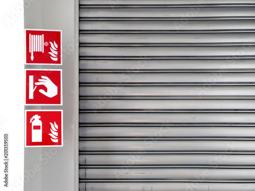 Real-use standard fire symbol labels, fire hose, fire switch, Dry Powder Fire Extinguisher, hanging in front of roll door of factory or warehouse