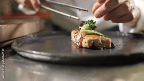 Hands chef finish off the dish. Slow motion. Chef at the white uniform to spread on large plate piece of meat, vegetables and seasonings, prepares to serve the client a restaurant, cafe or catering