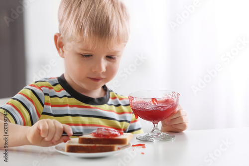Foto Cute little boy spreading jam on toast at home