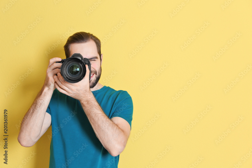 Young photographer with professional camera on color background - obrazy, fototapety, plakaty 