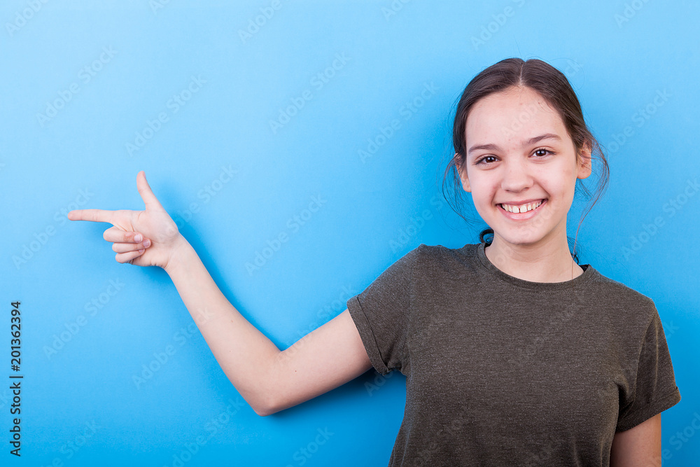 Young girl pointing on the side over blue background in studio photo Young girl pointing on the side over blue background in studio photo