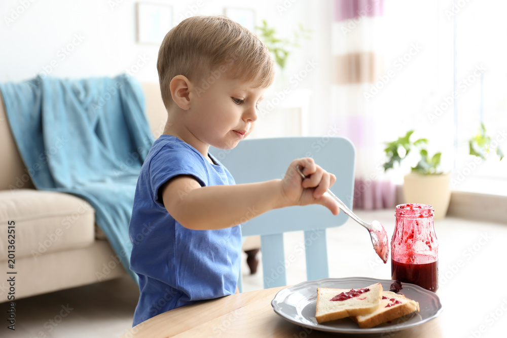 Little boy spreading jam on toasts at table in living room Little boy spreading jam on toasts at table in living room