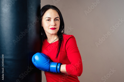 Portrait of a beautiful brunette woman exercising with boxing gloves on her hands in the gym. athlete with make-up red lipstick and dress boxing in the gym. the concept of women's power and feminism