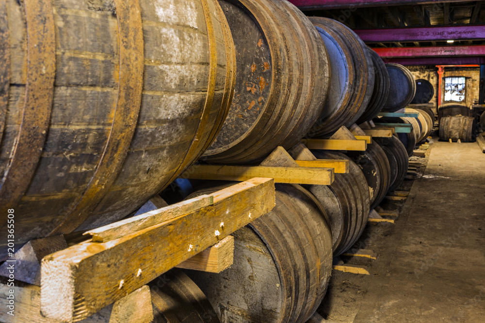 Stacked pile of old wooden barrels and casks in aging cellar at whisky distillery in Scotland