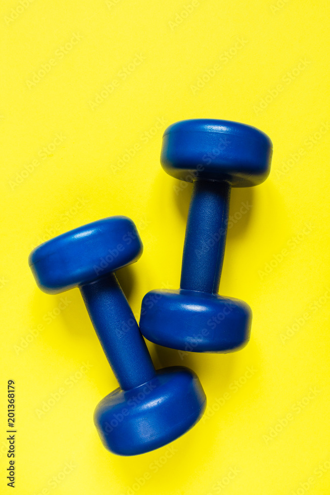 Blue dumbbells for sport and a bottle of water on a yellow background flat lay top view with copy space Blue dumbbells for sport and a bottle of water on a yellow background flat lay top view with copy space