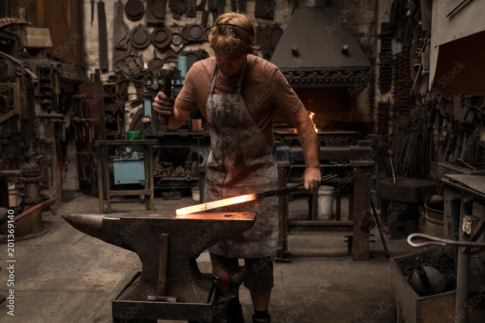 Blacksmith hammering a hot metal rod Blacksmith hammering a hot metal rod