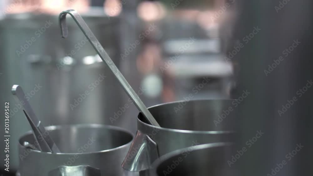 Cuisine of restaurant or cafe or hotel. Steam comes from pots, standing on stove or hob. Process of cooking. In the background chefs and staff at work. Boiling water in large saucepan. Spoon in pan.