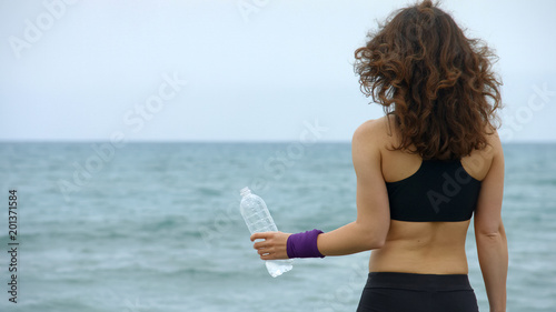 Young sportswoman with bottle on beach, feeling thirsty after workout, health photo