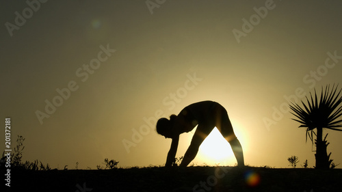 Female silhouette doing body stretching exercises, practicing yoga in sunlight © motortion