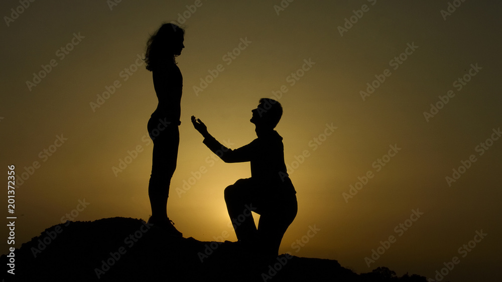 Man making proposal to woman at dawn in mountains, happy couple in love engaging