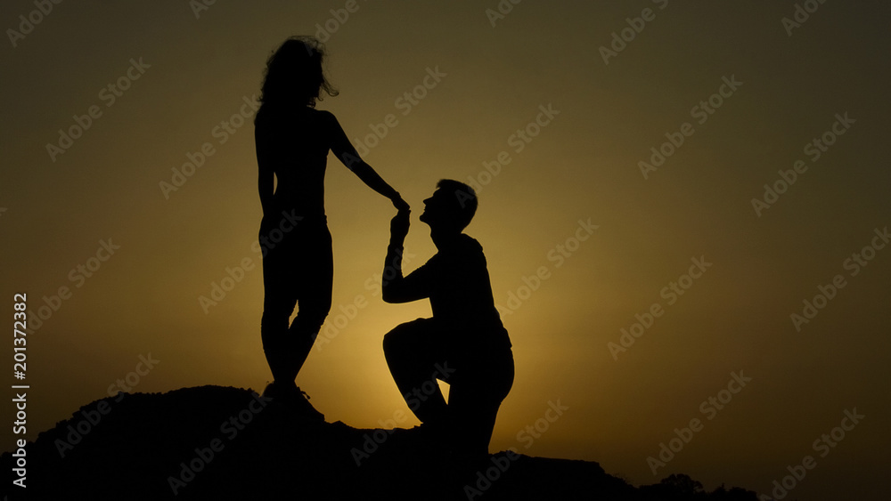 Silhouette of young man proposing to girlfriend on his knee, romantic engagement