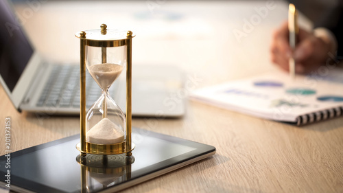 Time is running in hourglass, female manager checking graphs at office desk