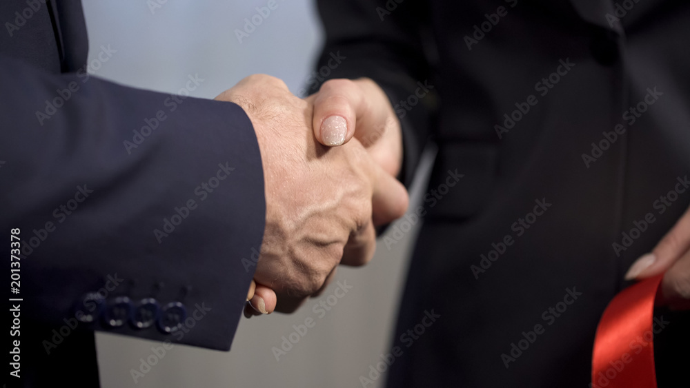 Top manager shaking hands with female business partner after ribbon cutting