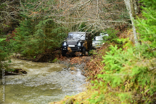 Offroad race in forest. SUV or offroad cars crossing water stream. Car racing with creek on way. Extreme driving, competition and 4x4 vehicles concept