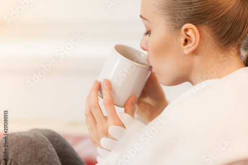 Woman lying on sofa under blanket drinking tea