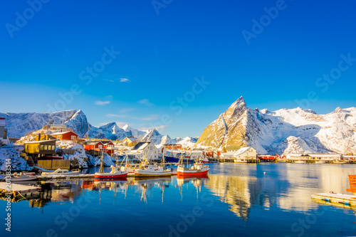 Above view of some wooden buildings in the bay with boats in the shore in Lofoten Islands surrounded with snowy mountains and colorful winter season