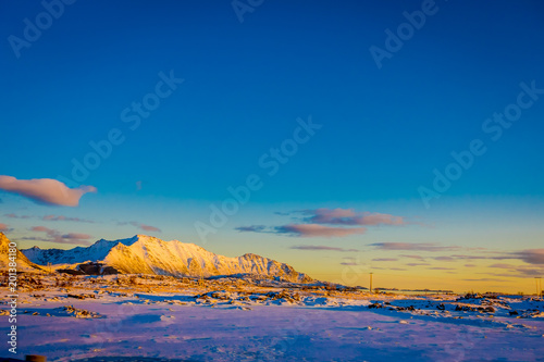 Sunset at Henningsvaer shoreline with huge mountains covered with snow in a gorgeous blue sky on Lofoten Islands, Austvagoya
