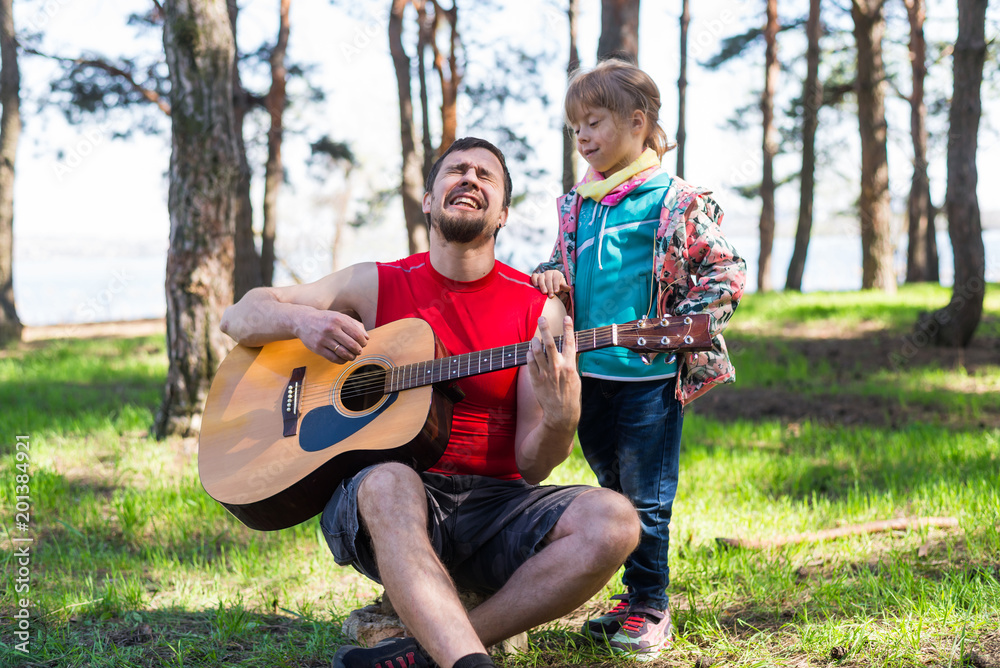 Fototapeta premium Family duet: Dad playing the guitar with his daughter, free space for your text.