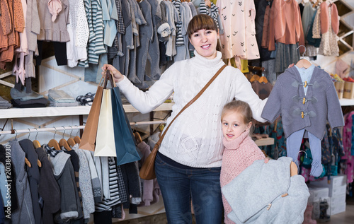 Pregnant mother and daughter choosing romper suit for baby in children’s clothes shop