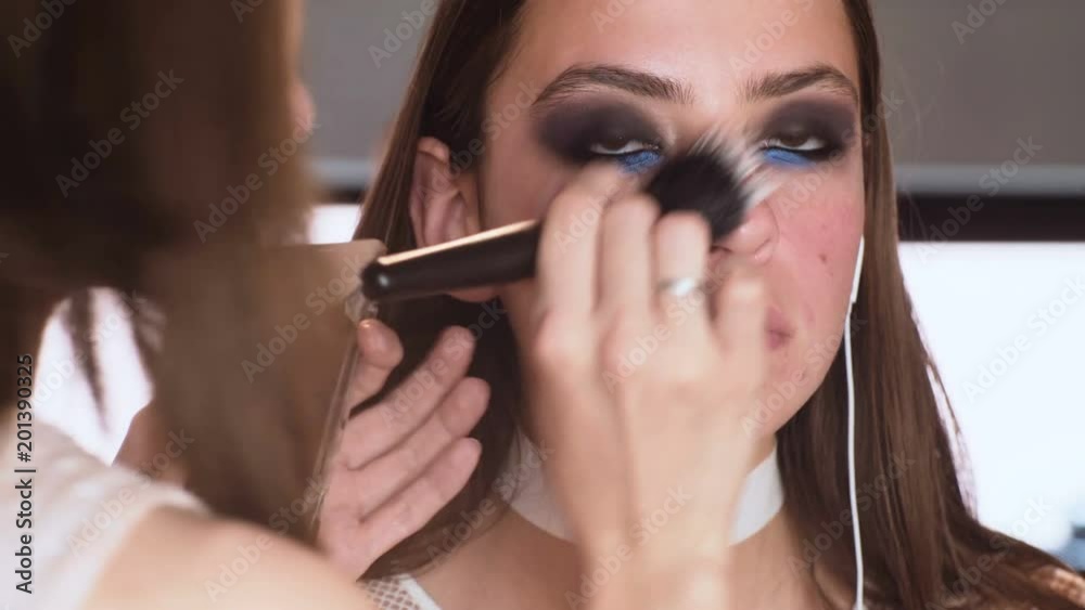Make-up artist applying the foundation to model. Close up. Makeup artist doing makeup for girl indoor. Make-up artist applying bright base color eyeshadow on model's eye. Make-up artist applying the foundation to model. Close up. Makeup artist doing makeup for girl indoor. Make-up artist applying bright base color eyeshadow on model's eye.